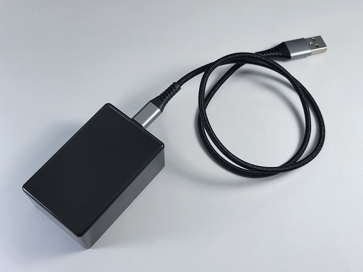 An ESP32 Services sensor, a small black box, with its braided USB cable.