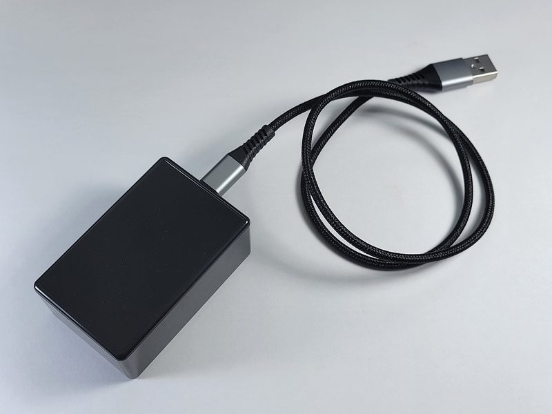 The ESP32 Services Activity Sensor, a small black box, with its braided USB cable.